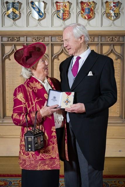 David Laing and his wife, Mary, are dressed smartly and gazing at each other as David holds out his CBE medal